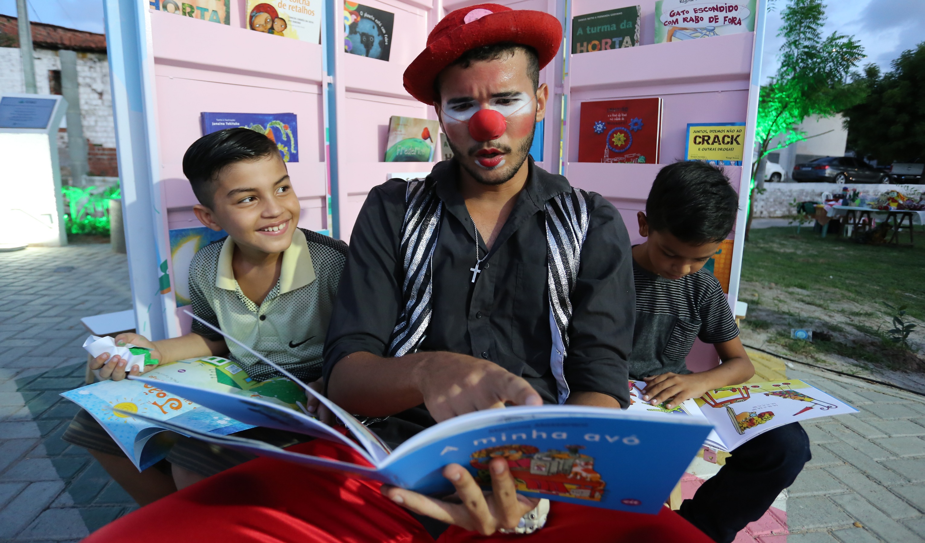 palhaço sentado, entre dois garotos, com livro no colo